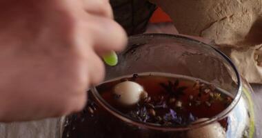 Hands make potion and put candy eyes and jelly worms in glass bowl of dark brew liquid with floating dried herbs and magic ingredients. Halloween and Day of the Dead props. Halloween potion making video
