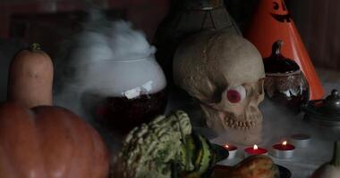 Hands make gestures to put spell over smoky potion in glass bowl with Halloween decorations and skull on table with tea lights candles. Person conjure with magic potion. Halloween witchcraft concept video