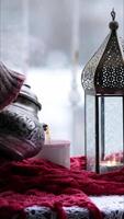 Ramadan lantern with tealight inside and hands pour hot tea from traditional teapot into mug wrapped in red scarf and steam rising. Arabic style vintage lamp and patterned metal kettle. Vertical video