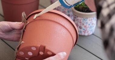 Hands apply glue to create a burlap decoration on a flower pot. This craft project enhances outdoor and indoor gardening with a rustic touch. Redecorating of flower pot using glue and burlap. video