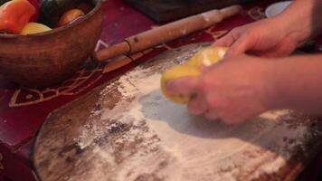 Knead and roll out dough by pressing with hands using rolling pin into square shape closeup. Kitchen board with flour, cookware, ingredients on table. Baking, cooking process, recipe of baking pie video