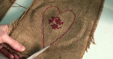 POV hands cut out decoration by heart shape using scissors. Making burlap heart craft for Valentines Day or Mothers Day. Handmade decoration made from burlap in traditional way. Step of crafting video