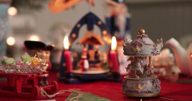 Christmas still life with rotating vintage music box on foreground and traditional nativity carousel and candles on blurred background. Holiday decorations and table centerpiece with candlelight video