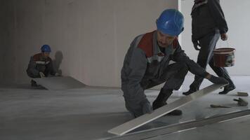 Workers in uniform and safety helmets lay tiles in a house construction video