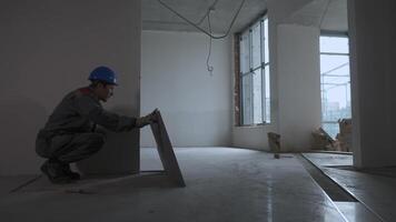 Worker laying tiles. In the next room, engineers are discussing the construction plan video