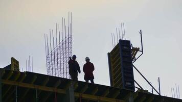 Silhouettes of an engineer and a worker on the roof of a house under construction assessing the work video