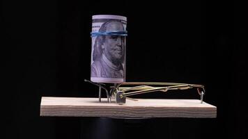 Mousetrap with roll of hundred dollar banknotes as bait on black background video