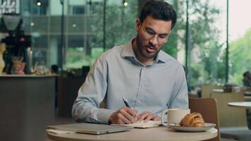Indian businessman Arabian man guy male business entrepreneur employee student writing in notebook studying in cafe customer write notes freelancer work learn tasks answer mobile call message reading video