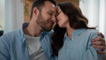 Cheerful beautiful young couple in love hugging cuddling relaxing on couch at modern home touch foreheads cuddle hug together feel love tender bonding affectionate enjoy romantic date wife husband photo
