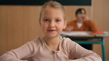 Caucasian clever happy little girl school test study task exam writing notes class lesson learn write copybook kid schoolgirl child pupil studying learning primary education smiling at camera at desk photo