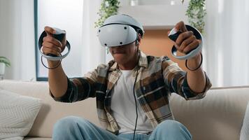 African American man having fun at home couch with virtual reality game fight guy play 3d cyber gaming fighting with controllers man playing in VR glasses helmet using joysticks metaverse world photo
