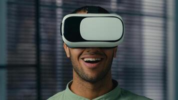 Close-up smiling latin american man wearing virtual reality glasses friendly showing invitation gesture asking to come welcome symbol making choice male player playing in cyberspace with vr goggles photo