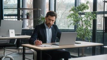 Focused adult businessman work on project in office using laptop writing notes caucasian man business leader professional employee analyze information on internet write data planning with computer app photo