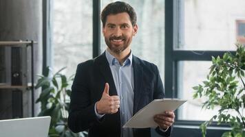 Focused adult caucasian man recruiting agent standing in office making notes writing checklist businessman conducts inspection write strategic plan showing thumb up gesture approval best choice sign photo