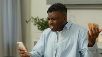 African American man biracial male ethnic guy user at home indignant confused angry bad sms news device problem mobile phone lost app crash smartphone read negative message annoyed gadget trouble spam photo