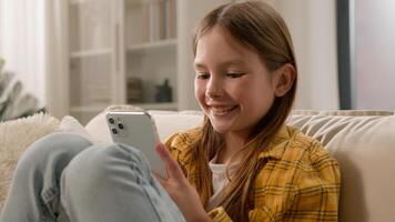 Smiling happy kid girl sending message checking email using mobile phone cute schoolgirl child chatting with friends on social network internet playing online game watching on smartphone at home photo