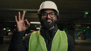 Happy Indian technician contractor mechanic in hardhat helmet showing ok gesture parking lot recommend okay sign factory work Arabian man worker manufacture engineer in hard hat heavy metal industry photo