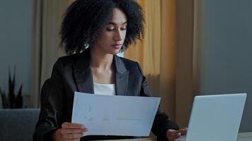 African teacher worker business woman work with graphics documents at home office check documentation enter financial data to laptop processing online information paying bills in computer banking app photo
