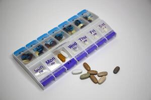 Weekly pill organizer with supplements and medications on white background. photo