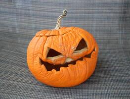 Wrinkled carved pumpkin with a spooky expression on a fabric background. photo