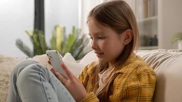 Smiling happy kid girl sending message checking email using mobile phone cute schoolgirl child chatting with friends on social network internet playing online game watching on smartphone at home photo