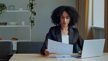 African teacher worker business woman work with graphics documents at home office check documentation enter financial data to laptop processing online information paying bills in computer banking app photo