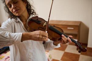 Woman playing violin with closed eyes in peaceful home environment photo