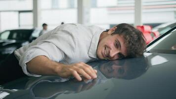 Happy Caucasian man driver buyer excited guy client in auto automobile salon choose new auto stroking car hood hugging cuddling lying on vehicle buying transport enjoy purchase test drive rent service photo