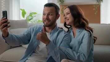 Caucasian happy couple family waving hello showing thumb up talking conversation virtual call mobile phone conference chat blog vlog in social media bloggers speak at home with smartphone app photo