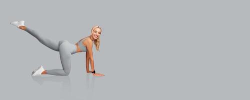 A fitness enthusiast is engaged in a lower body exercise, lifting one leg while on hands and knees. She wears comfortable workout clothing and has a focused expression, suggesting determination. photo