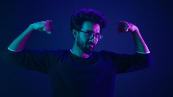 Proud slim weak Arabian man coder guy technology hacker show hands muscle bicep sport strong power like bodybuilder neon studio background champion boast efficient security coding achievement level up photo