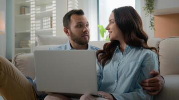Happy young couple using laptop for ecommerce doing online shopping with shop app together at home Caucasian man and woman looking at computer buying searching in internet booking trip tickets choose photo