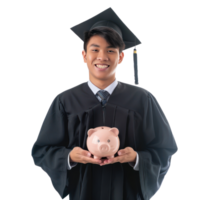 Smiling young man wearing graduation gown uniform standing with hand holding piggy bank isolate on transparency background png
