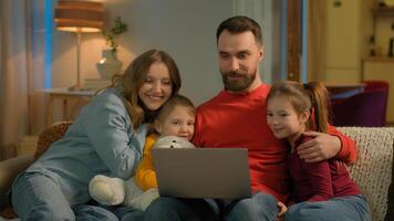 Caucasian family parents children on couch evening home teach little girls using pc laptop mom dad help daughters siblings kids computer e-learning education custody online shopping parental control photo