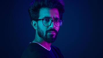 Indian man guy profile turning head looking camera serious developer coding internet technology hacker programmer Arabian male in glasses neon blue ultraviolet studio background high-tech cyberspace photo
