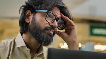 Indian bearded stressed man in glasses working at office with laptop Arabian businessman sad with business problem failure head pain suffering from chronic severe headache thinking trouble solution photo
