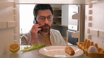 Point of view POV inside refrigerator Caucasian male man guy open fridge with one egg lettuce leaf piece of bread crumbs empty bottle of juice talking phone order products call food delivery service photo