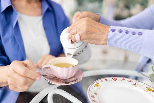 dos mayor mujer son compartiendo un encantador momento a un cafetería, como uno vierte té dentro un delicado taza. ellos abrazo un relajado estilo de vida, disfrutando cada otros empresa en Jubilación. foto