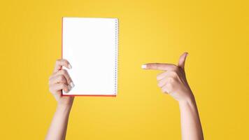 Woman pointing at empty notebook on light background, closeup. Mockup for design photo