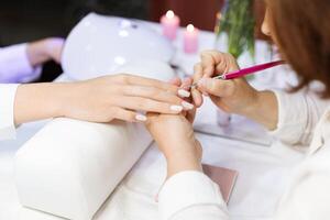 Ladies indulge in a relaxing manicure at a salon, with one woman receiving nail art while candles create a calming atmosphere. The focus is on vibrant nails and attentive service. photo