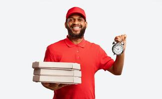 Pizzeria Courier Delivering Pizza On-Time Holding Boxes And Clock Smiling To Camera Posing Over Yellow Studio Background. photo
