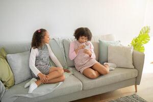 Two young daughters enjoy quality time in their cozy living room, engaging with each other and sharing smiles while seated on a comfortable couch. The atmosphere is filled with warmth and love. photo