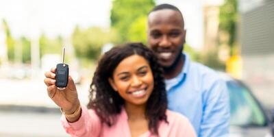 Buying New Car. Happy Black Woman Showing Keys Of Her Automobile, Man Embracing His Wife, Using Auto Rental Service, Lady Celebrating Receiving Drivers License, Smiling And Looking At Camera photo