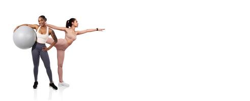Two women are participating in fitness exercises. One balances a stability ball while the other stretches in a yoga pose, demonstrating strength and flexibility. The background is minimalistic. photo