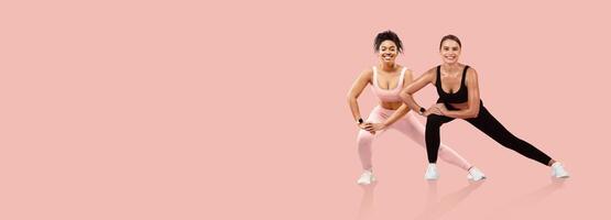 Two women engage in a workout routine, showcasing teamwork and motivation. They wear vibrant activewear and demonstrate an exercise on a pastel pink background, emphasizing fitness. photo