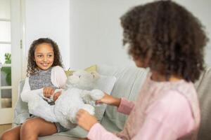 Sisters share a playful moment on the couch as they engage with a soft toy, showcasing love and affection in their comfortable family home environment. photo