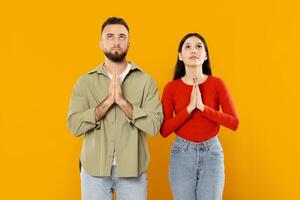 A young Caucasian couple stands side by side, their hands clasped together in a gesture of love and devotion. The vibrant yellow background enhances their connection and warmth. photo