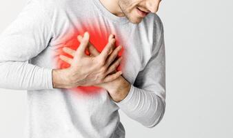 Problems with heart. Man feeling chest pain, presses his hands to highlighted in red place, panorama, cropped, studio shot photo