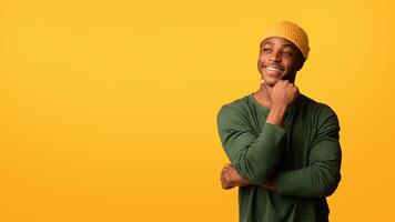 Nice Offer. Portrait Of Thoughtful Black Hipster Guy Looking Aside At Copy Space With Interest, African American Man Touching Chin, Thinking About Something While Standing On Yellow Background photo