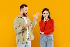 A young couple stands together, with the man expressing frustration through gestures while the woman appears contemplative. They are isolated, highlighting their emotional exchange. photo